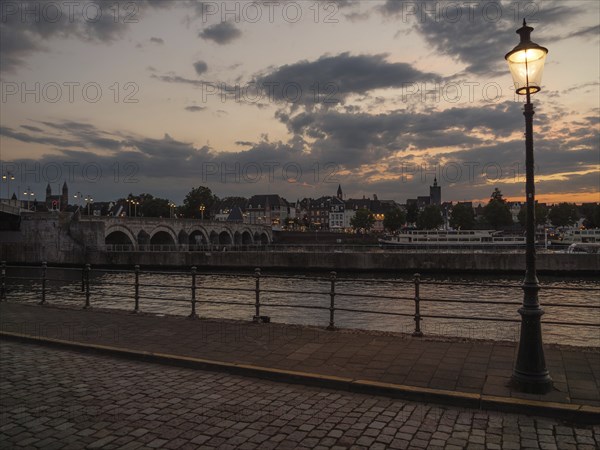 Riverbank at dusk with a street lamp and a cobblestone walkway, Maastricht, limburg, the