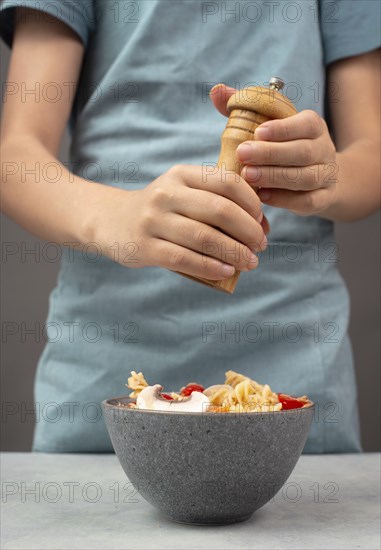 Putting pepper in a pasta salad, sliced mushroom, tomato, red pepper pieces and tuna, healthy food