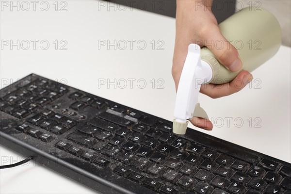 Cleaning computer keyboard in office, spraying water with a spray bottle dusty and dirty
