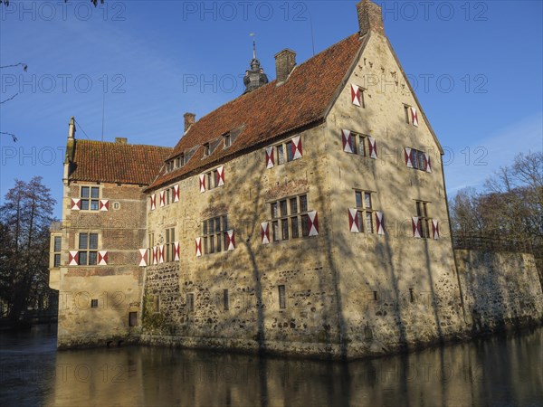 An old moated castle with red shutters and a red roof, surrounded by water, lüdinghausen,