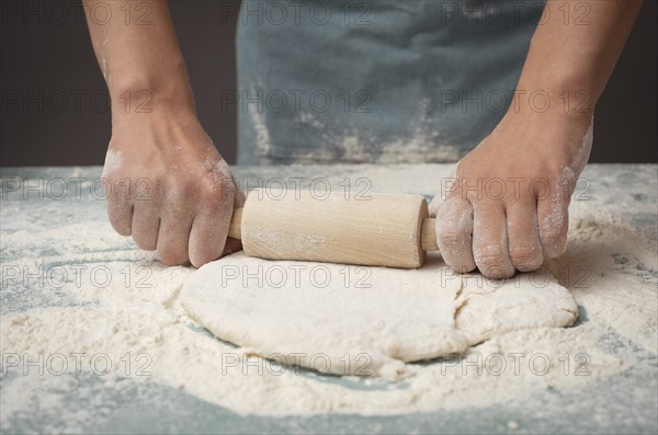 Baker rolls out dough for pizza, flatbread or pastry with rolling pin, prepare ingredients for