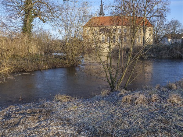 Historic building with a red tiled roof on the riverbank, surrounded by bare trees and a wintry