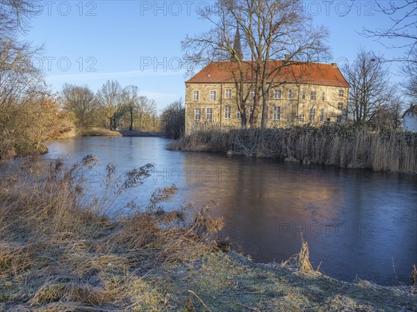 Historic building with red tiled roof on the riverbank, surrounded by bare trees in a wintry