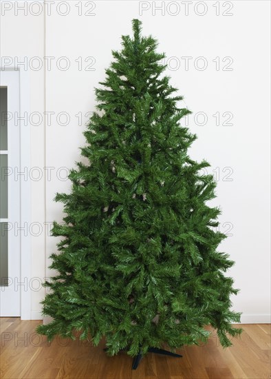 Bare artificial christmas tree in house with white furnishings and oak parquet flooring