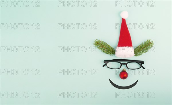Face of a reindeer with a red bauble nose, fir antlers, a santa claus hat and eyeglasses, merry