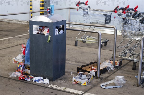 Overflowing dumpster, trash can with plastic bags and cardboard, filthy shopping center,