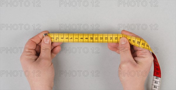 Hand holding yellow tape measure, fitness and diet concept, control with measurement