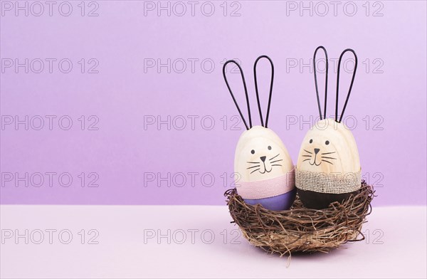 Easter bunny or rabbit couple cuddle together in a wicker nest, wooden egg, spring holiday greeting