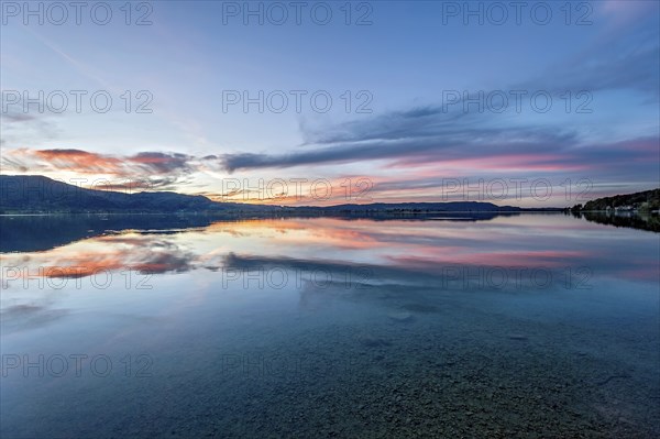 Lake Kochel with reflection of sun and clouds at sunset, calm water, in the background the