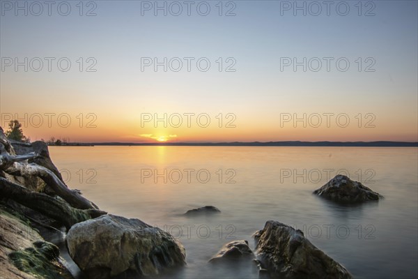 Sunset on the shore of a lake in summer. Colourful sky with a wide view of the horizon. Natural