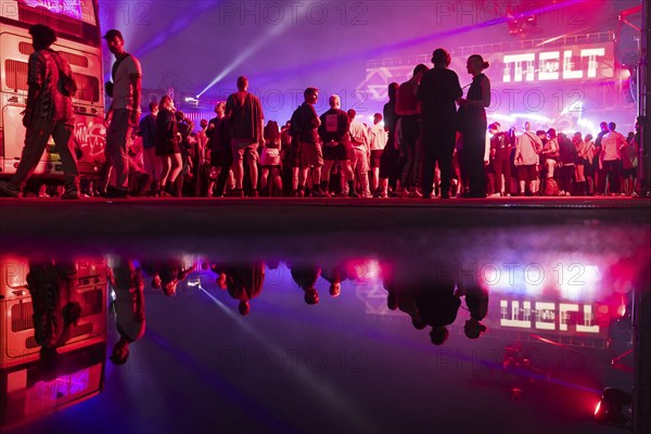 Festival visitors are reflected in a puddle at the Melt Festival in Ferropolis on 12 July 2024.