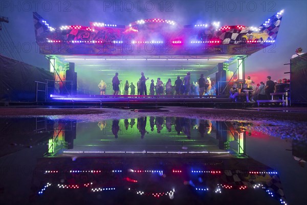 A bumper car with dancing visitors is reflected in a puddle at the Melt Festival in Ferropolis on