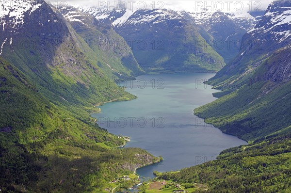 Impressive lake framed by high mountains and dense forests under a cloudy sky, Lovatnet, Loen,