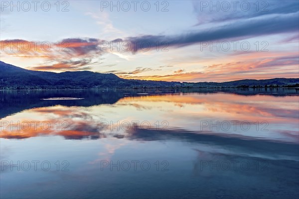 Lake Kochel with reflection of sun and clouds at sunset, calm water, in the background the