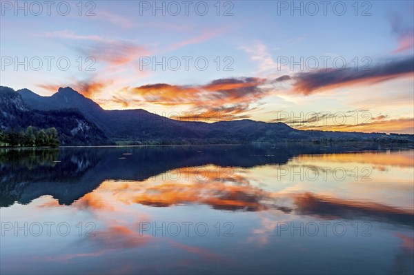 Lake Kochel with reflection of sun and clouds at sunset, calm water, behind the mountains Stein,