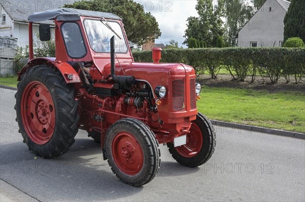 Red vintage tractor, carefully restored oldtimer, driving on the road through the village, motion