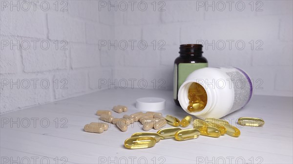 Vitamin and supplement capsules spilled on a white table with brown and white pill bottles