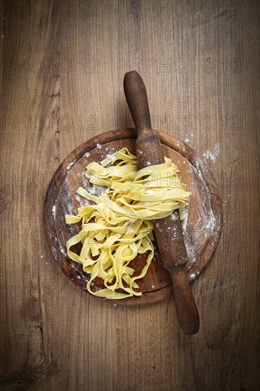 Raw tagliatelle pasta, homemade, on a rolling pin, top view, on a cutting board, cooking concept