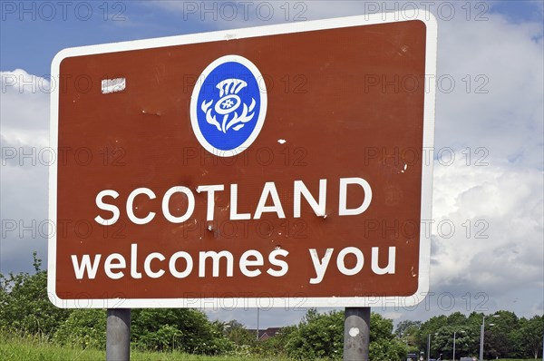 Brown sign with the inscription 'Scotland welcomes you' against a background of trees and cloudy