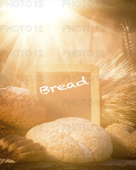 Bread and wheat on the wooden table in autumn field. Blackboard with copyspace