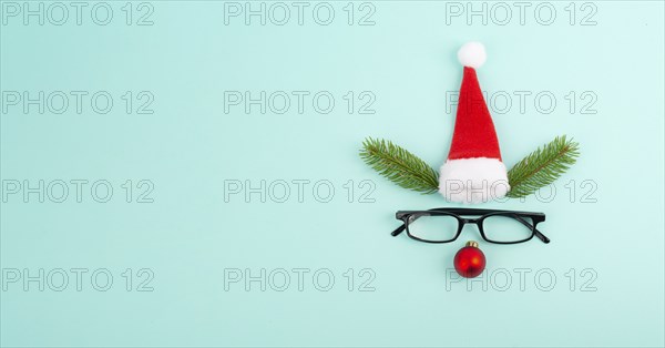Face of a reindeer with a red bauble nose, fir antlers, a santa claus hat and eyeglasses, merry