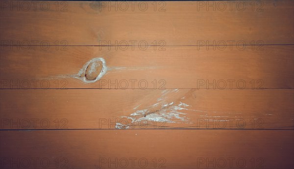 A close-up of orange-brown wooden planks with a noticeable knot and scratches, showcasing a rustic