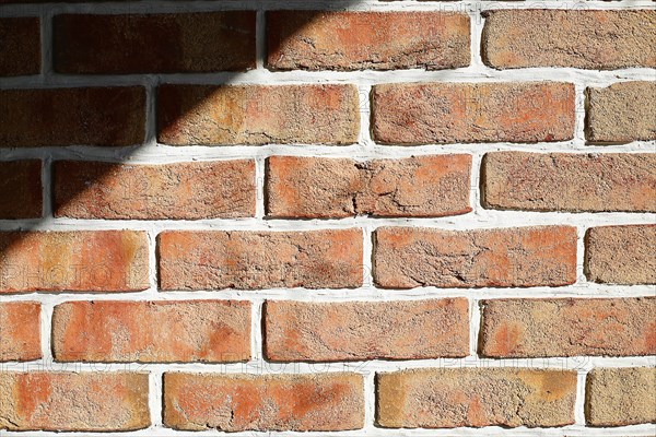 Sunlight and shadow on a textured red brick wall with white mortar, background image