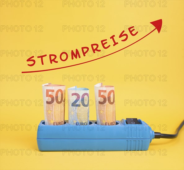 Euro banknotes in a power outlet, increasing prices for electricity is standing in german language