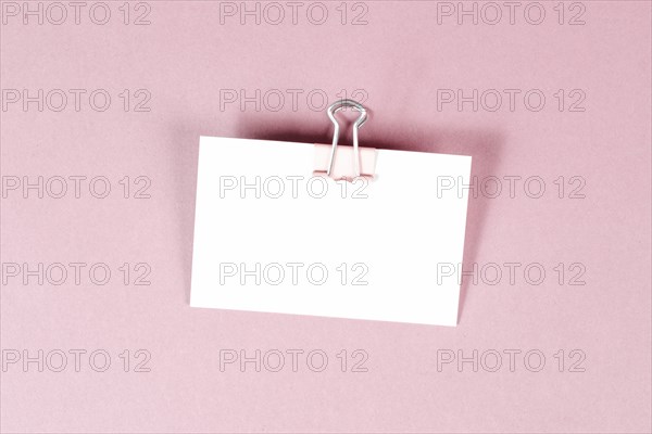Blank white paper with a paperclip on a pink colored background, copy space for text, reminder or