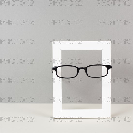 Home interior poster mock up with wooden frame and eyeglasses, gray wall background, copy space for