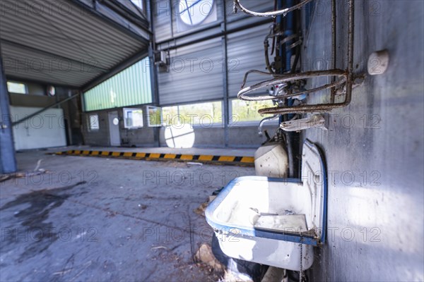 Abandoned hall with metal walls and an old washbasin in the foreground, demolition site,