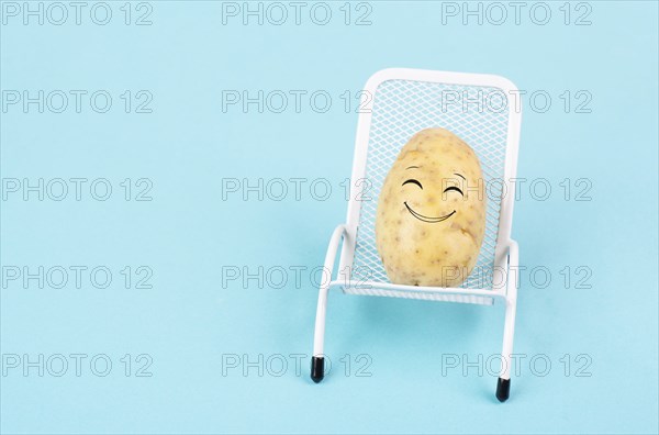 Potato with a funny face is sitting in lounge chairs, happy holiday, greeting card