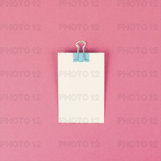 Blank white paper with a paperclip on a pink colored background, copy space for text, reminder or