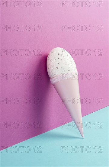 Ice cream cone with an egg, pink and blue background, copy space, easter holiday, summer season,