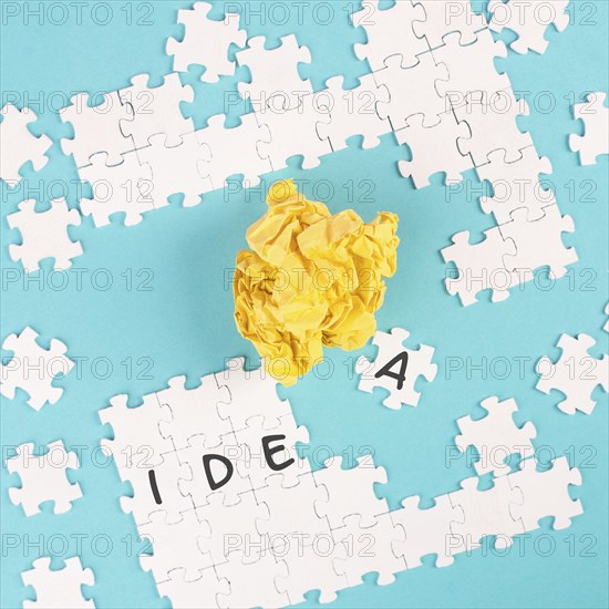 Puzzle on a blue background, yellow crumbled paper, word idea is standing on the jigsaw pieces,