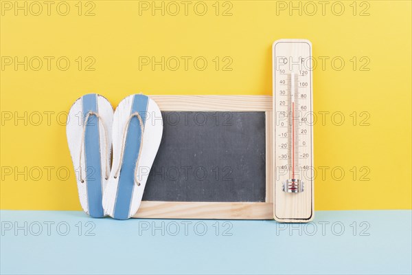 Empty chalkboard with a thermometer and flip flops, holiday background, summer vacation, hot