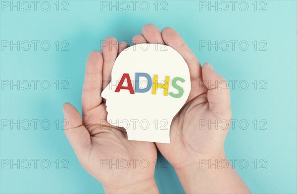 Hands holding a head with the german word ADHS which means attention deficit hyperactivity