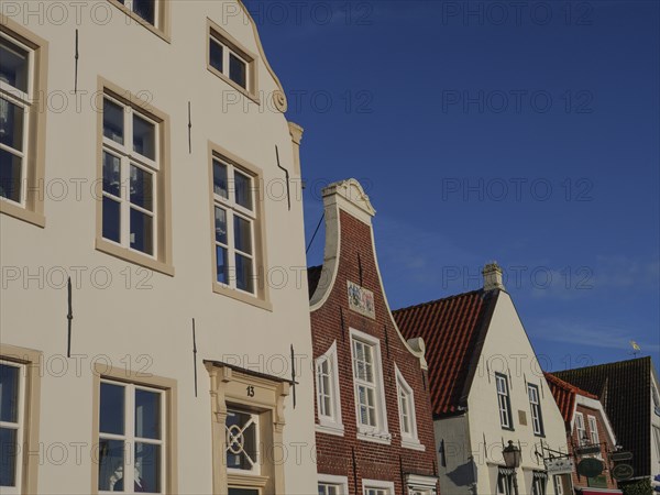 Close-up of various house facades with white and brick fronts under a cloudless sky, greetsiel,