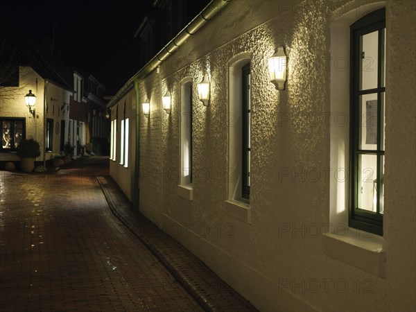 A dark street at night with white, illuminated buildings and cobblestones under streetlights,