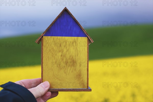 Holding a house in the hand with the colors of the ukrainian flag, home for refugees from Ukraine,