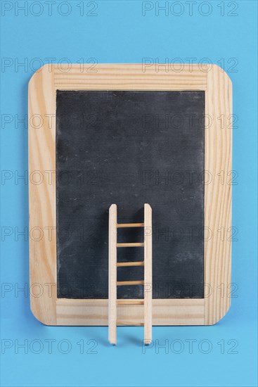 Ladder on an empty chalkboard, blue colored background, copy space, education, success, creative