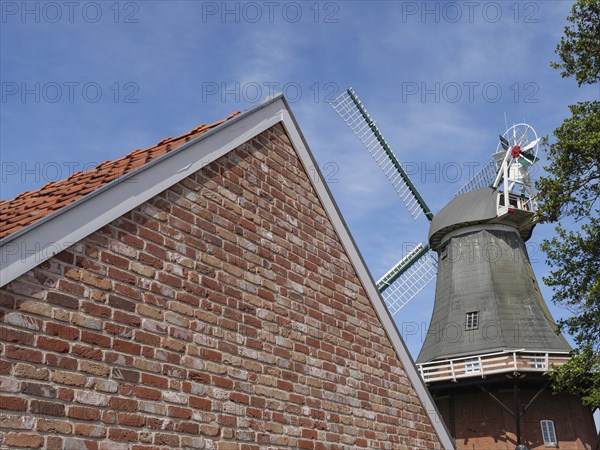Brick building with the top of a windmill in the background under a blue sky, Greetsiel, East