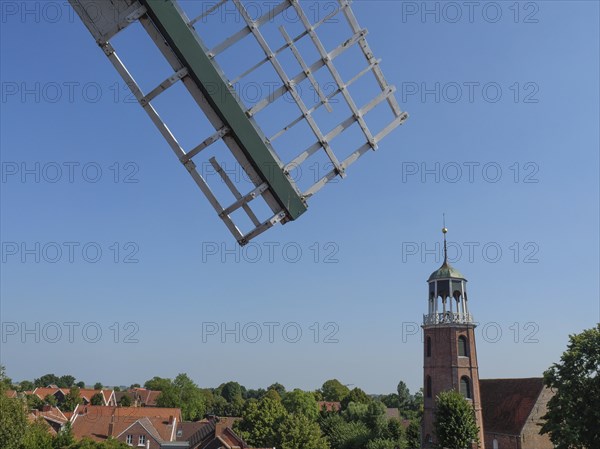 Parts of a windmill and a church tower rise above the roofs of a quiet village, Ditzum,
