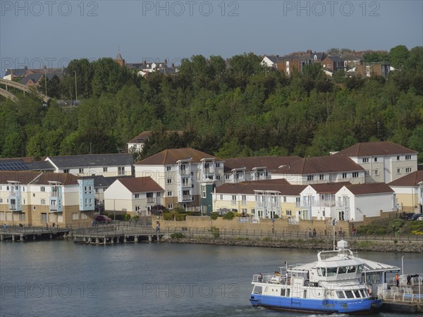 Residential area with a ferry in the foreground, surrounded by green spaces and the harbour,