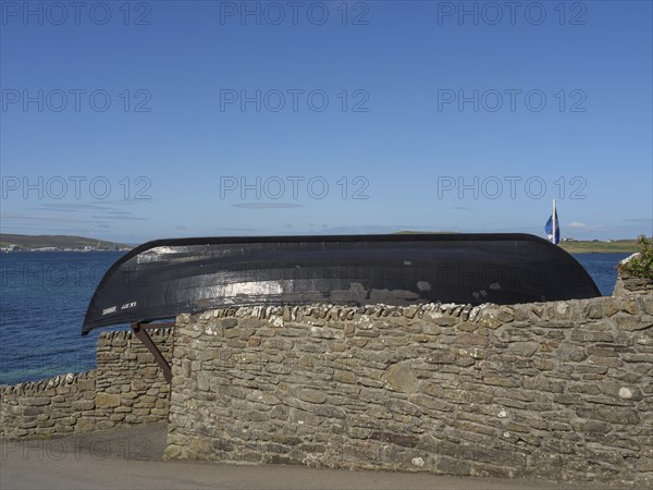An old black boat rests on a stone wall with sea views and clear skies, lerwick, shetlands,