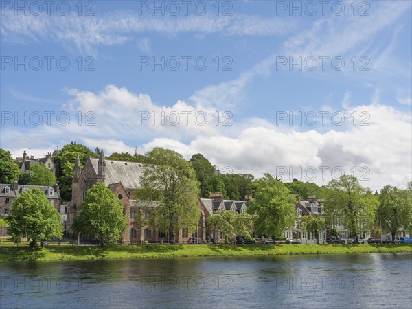 View of a picturesque row of houses and a church along a river with blue sky and white clouds,