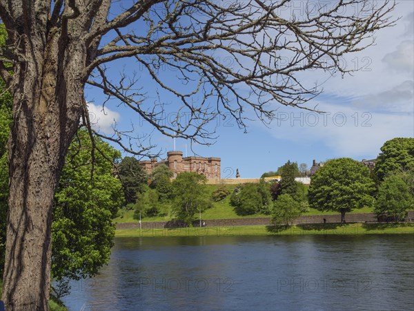 A castle on a hill on the banks of a river, surrounded by trees and under a blue sky, inverness,