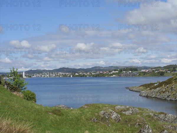 A calm lake surrounded by green hills and houses under a partly cloudy sky, haugesund, norway,