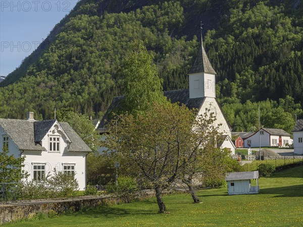 White church building in a green village, surrounded by trees and mountains, on a sunny spring day,