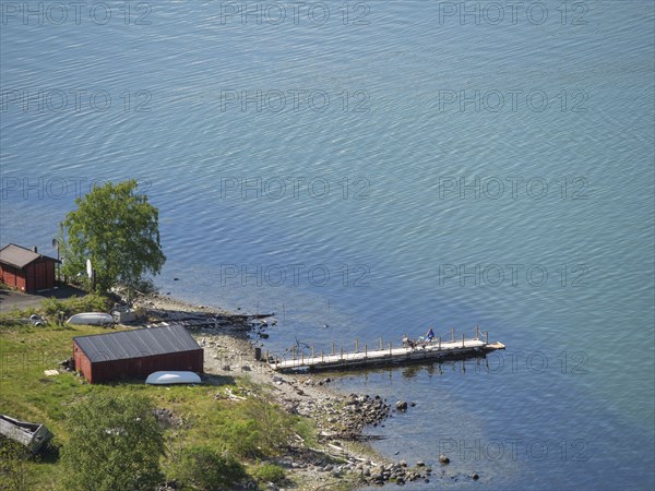 Calm lake scene with jetty and small red huts on the shore, clearly depicted water and nature,
